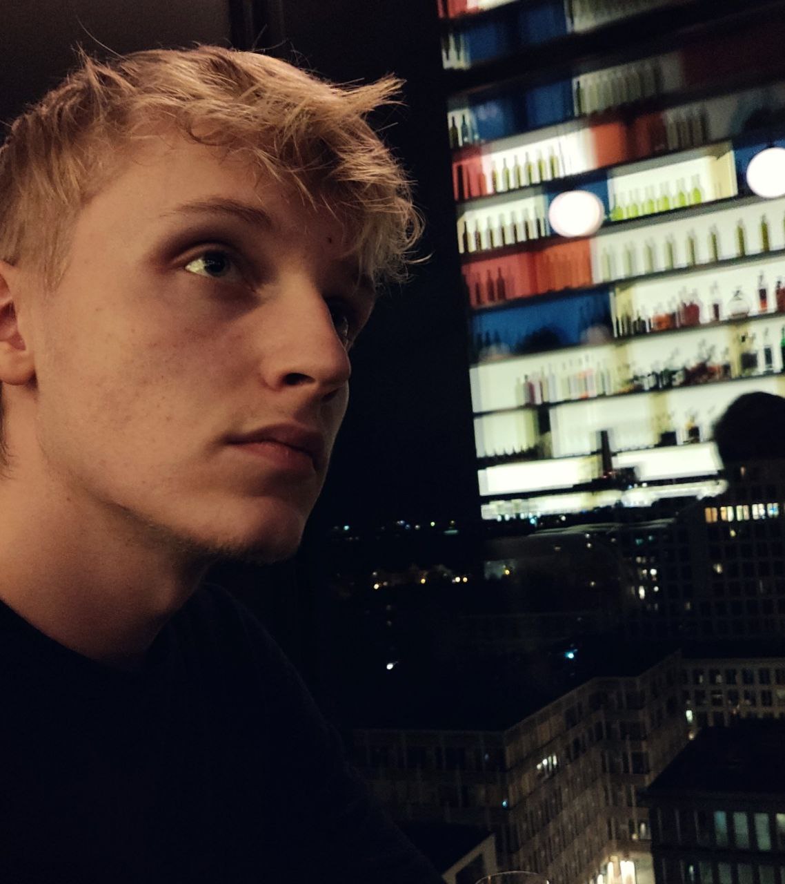 Ein gut aussehender, blonder, junger Mann, der nachdenklich in die Ferne blickt und einen schwarzen Pullover trägt